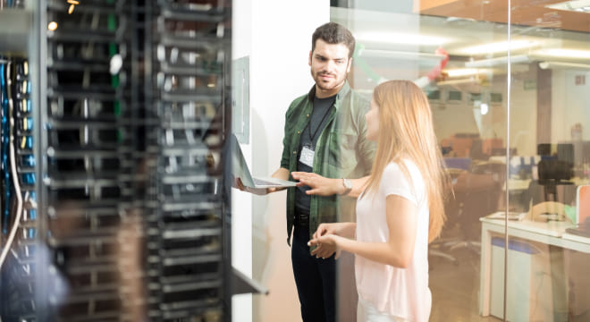 Two people standing in server room with laptop and discussing Data Migration